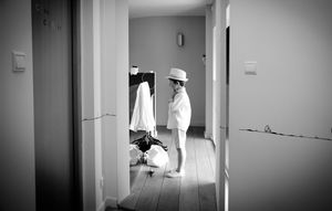 A person in white attire stands in a hallway looking at their reflection in a mirror.