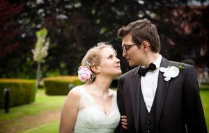 A couple in formal wedding attire embraces while walking through a garden setting.