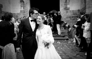 A joyful wedding celebration with guests throwing confetti over the newlyweds outside a historic stone church.