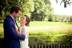 A romantic wedding couple embraces in a lush green meadow on a sunny summer afternoon.