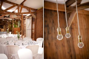 Rustic wedding reception venue with white tablecloths and hanging lightbulbs in a wooden barn-style interior.