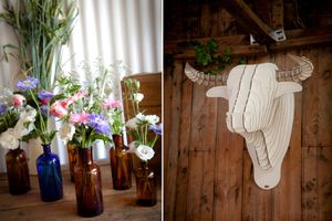 Rustic wedding decor featuring wildflowers in blue glass bottles and a white cardboard cow head mounted on wooden wall.