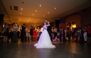 A couple shares their first dance at a wedding reception while guests watch from the edges of a dimly lit ballroom.