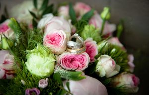 Close-up view of pink roses and white flowers arranged in a delicate floral bouquet with fresh green foliage.