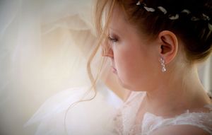 A delicate white wedding dress with intricate lace details hangs elegantly against a light background.