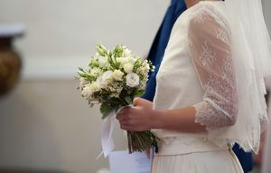 A wedding couple holds a delicate white and green floral bouquet against formal attire.