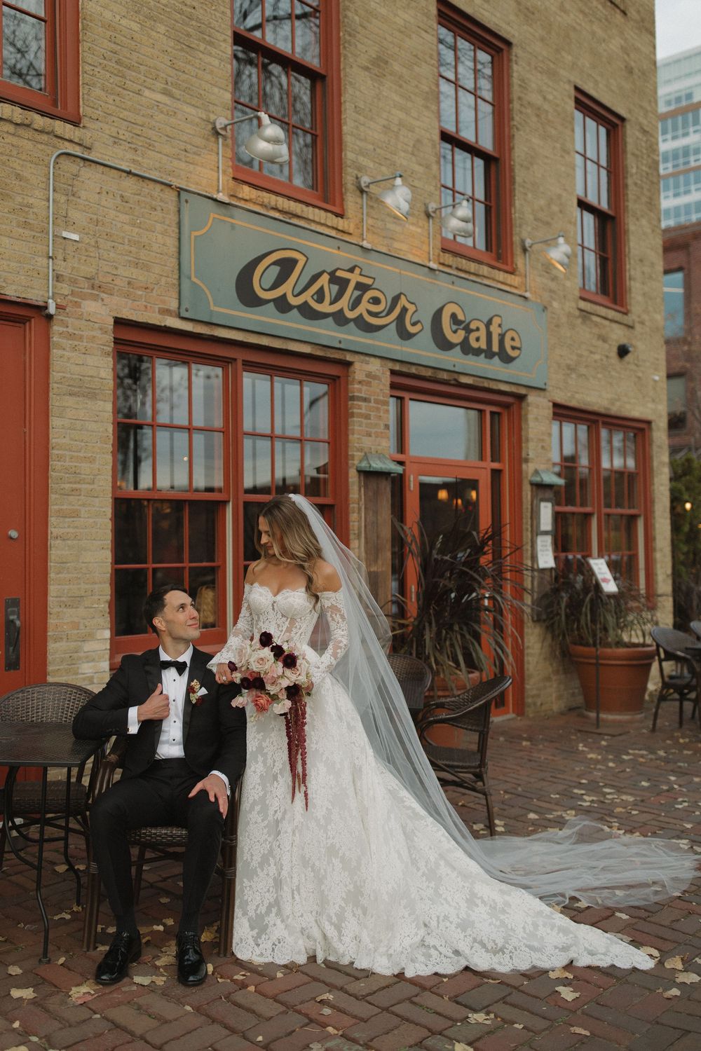A romantic wedding photo outside a brick building with the Aster Cafe sign, featuring a couple on a cobblestone patio.