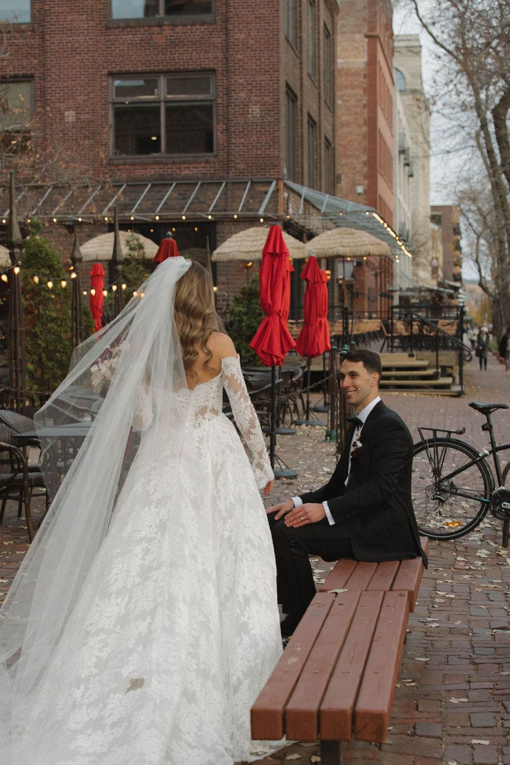 A series of wedding photos showing a couple sitting on a wooden bench outside a brick building with red umbrellas.