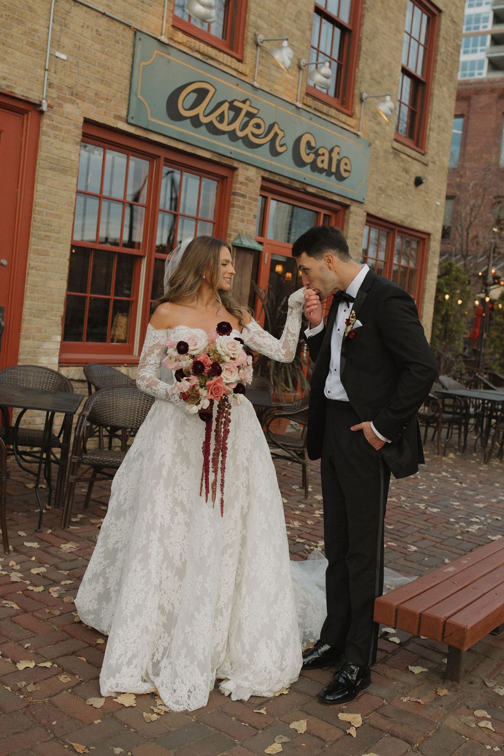 A joyful wedding couple laughs together outside a rustic Aster Cafe with red brick walls.