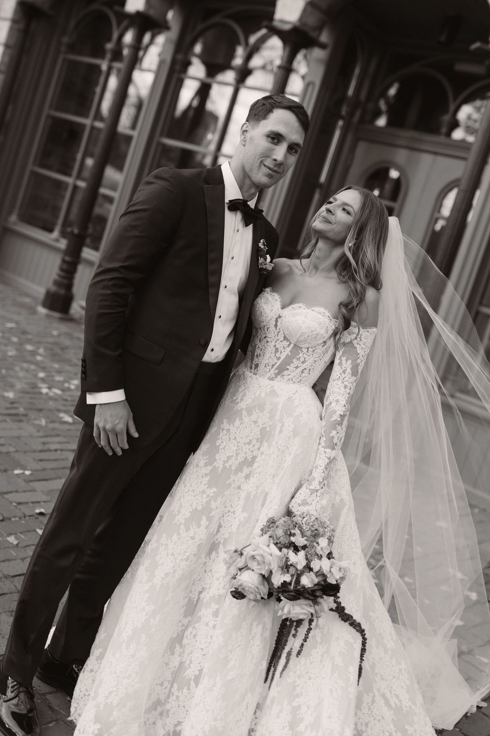 A stunning white wedding dress with intricate lace detailing and flowing veil on a cobblestone path.