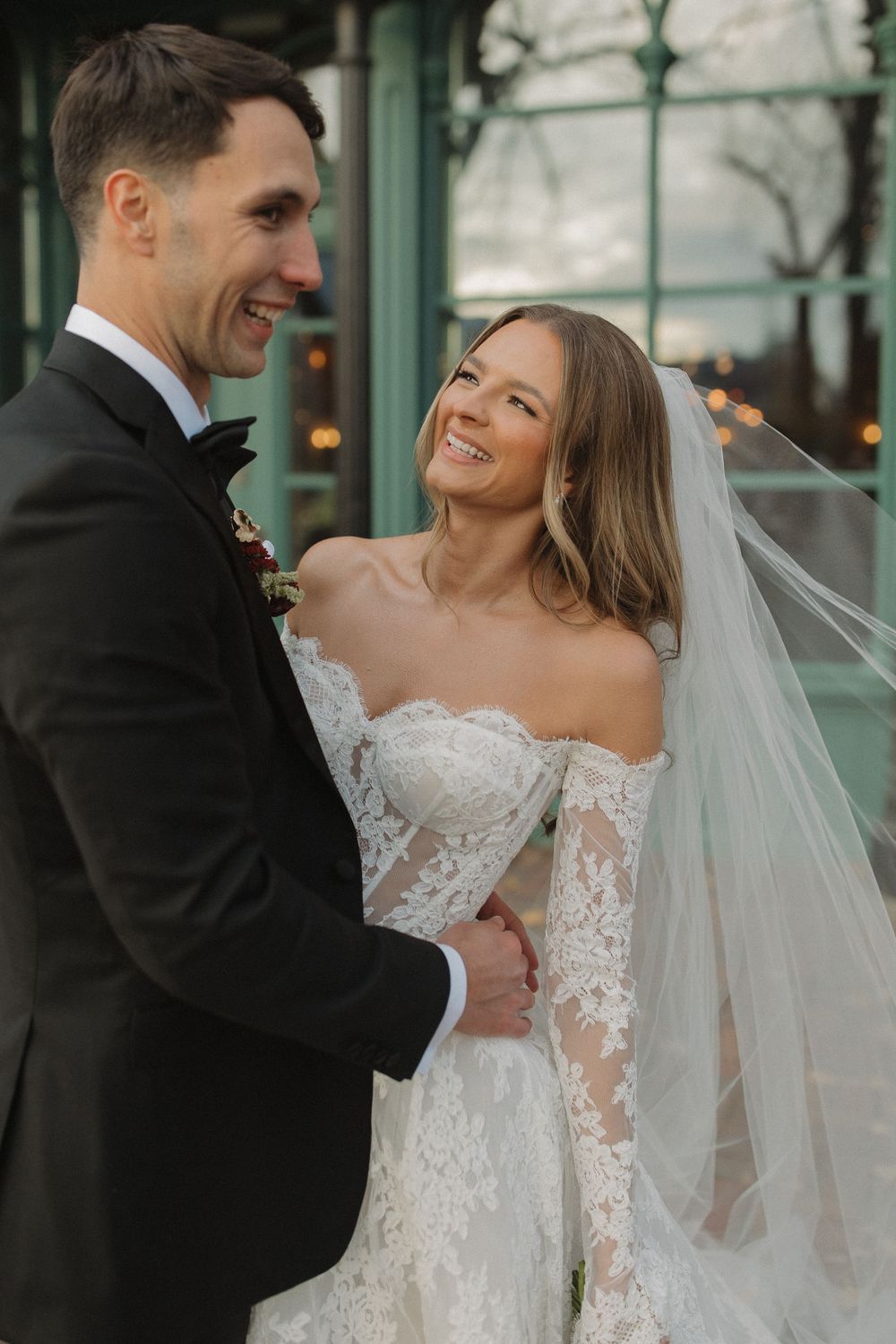 A joyful bride in a lace wedding dress shares a candid moment with her groom outdoors.