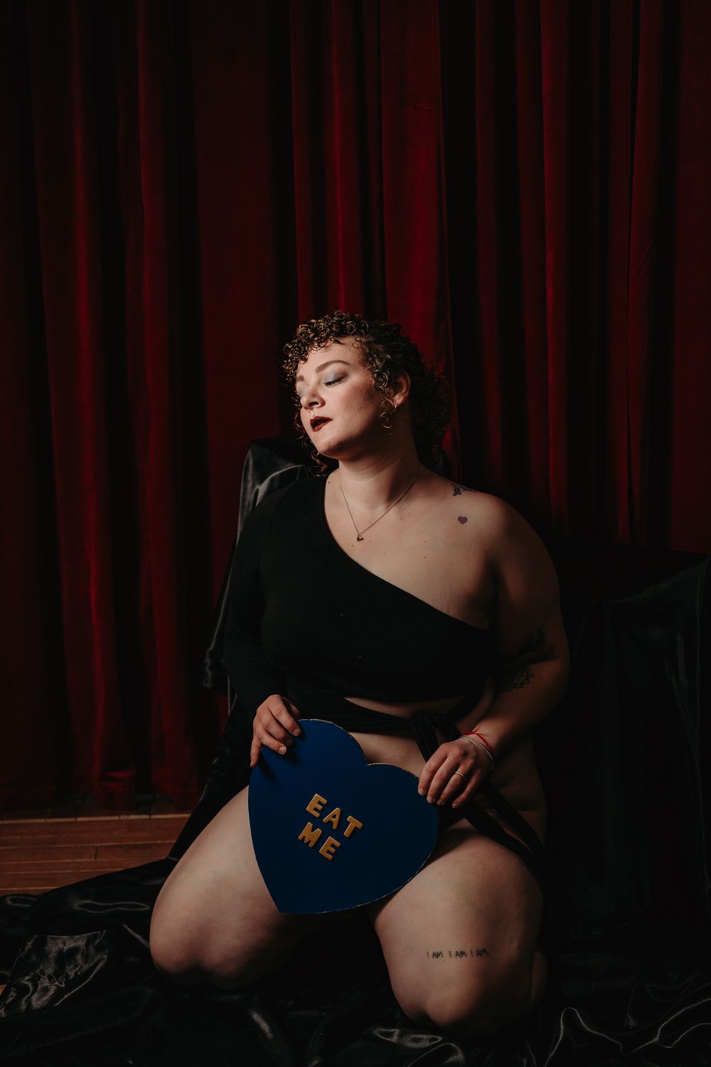 A moody boudoir photoshoot against dark red curtains in dramatic lighting.