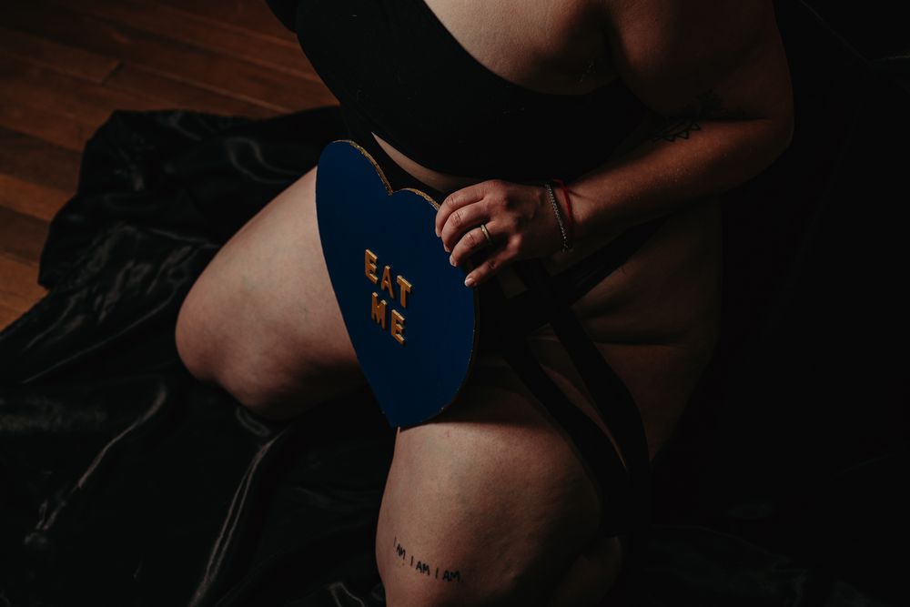 A person holds a blue fitness ball while exercising on a dark wooden floor.
