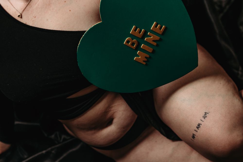 A person wearing a dark green baseball cap with gold lettering sits in a dimly lit setting.