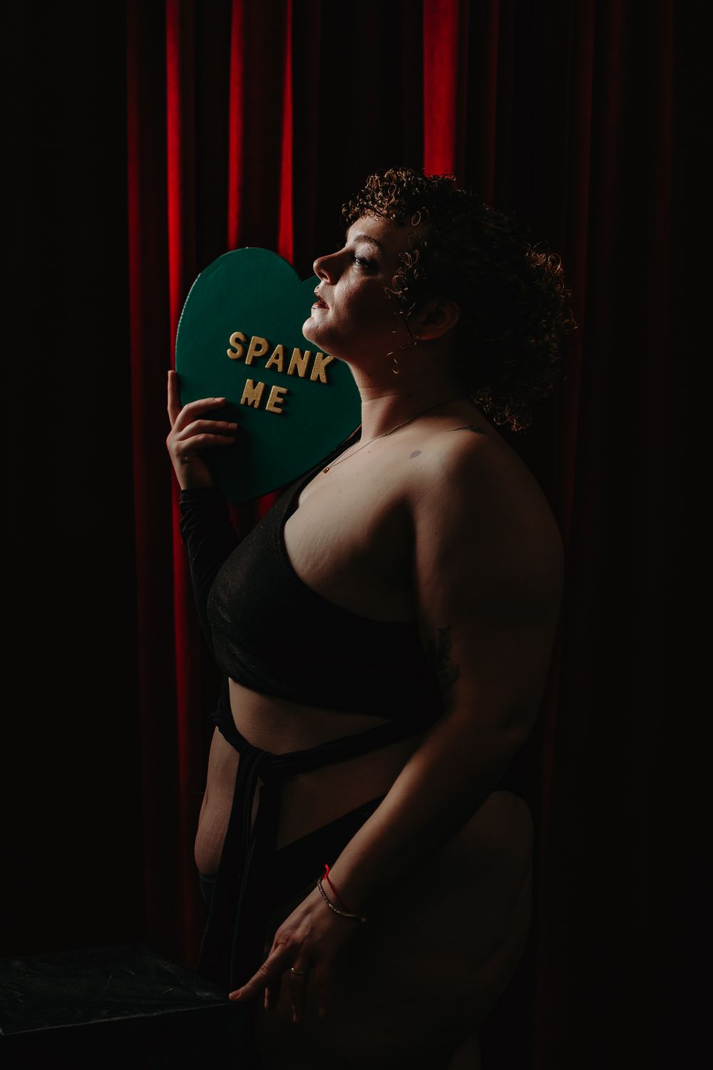 A series of dark moody portraits against a red curtain backdrop showing someone wearing a green baseball cap.