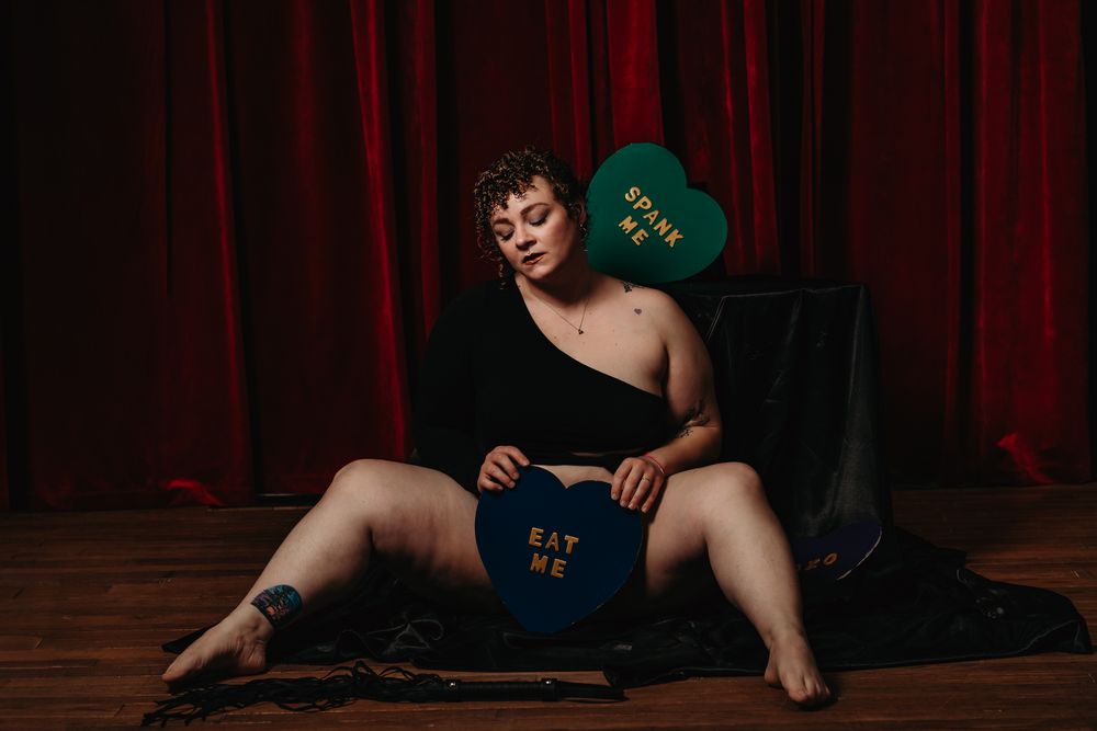 Boudoir photography setup with red curtains, wooden floor, and heart-shaped props in a moody studio setting.