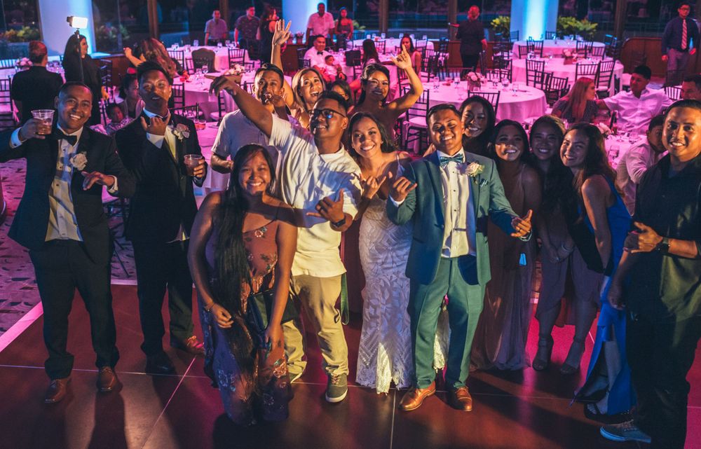 Crowded dance floor with party guests dancing under colorful lighting at an indoor celebration.