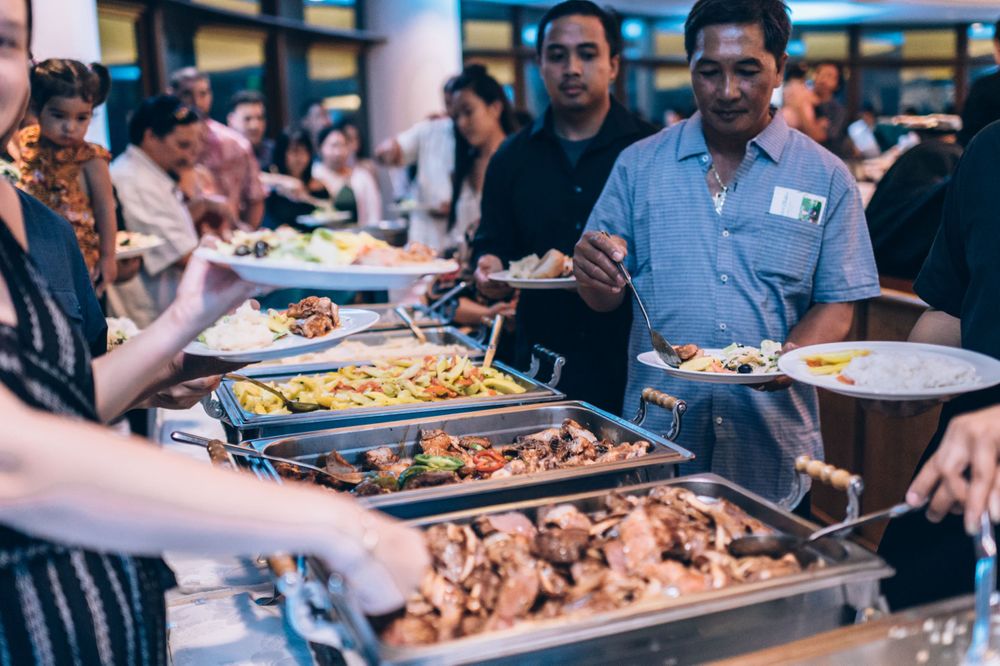 Buffet style catering setup with chafing dishes and guests serving themselves at an indoor event.