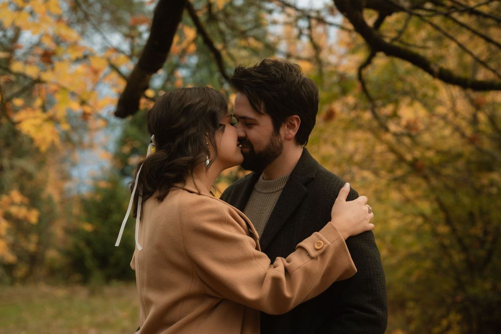 A romantic couple embraces in a wooded area with golden autumn foliage creating a warm backdrop.