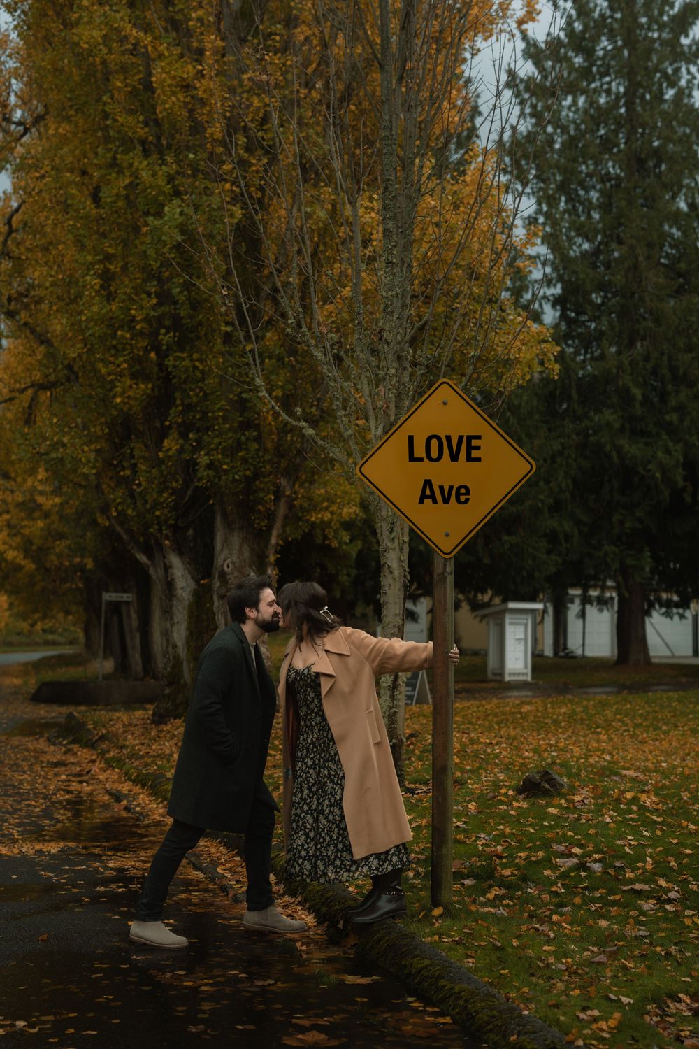 Couple playfully posing near a Love Ave street sign surrounded by fall foliage.