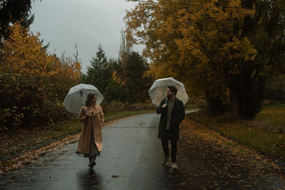 Two people with umbrellas walk along a misty autumn path surrounded by golden foliage.
