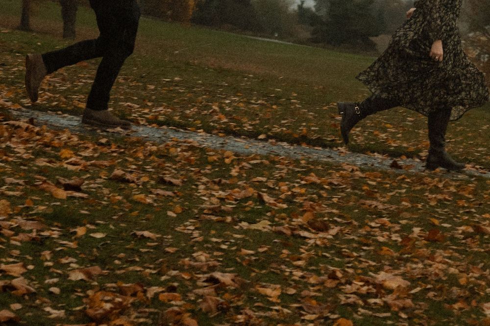 People walking through a park covered in golden autumn leaves on a cloudy day.