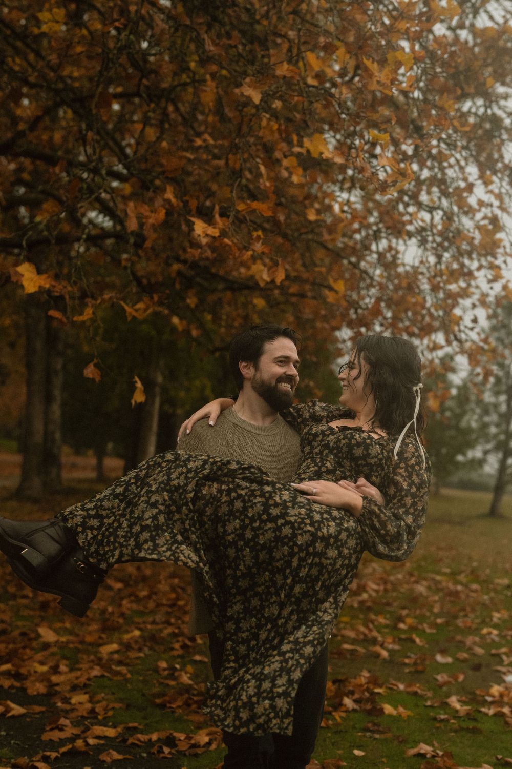 A couple embraces and dances together among fallen autumn leaves.