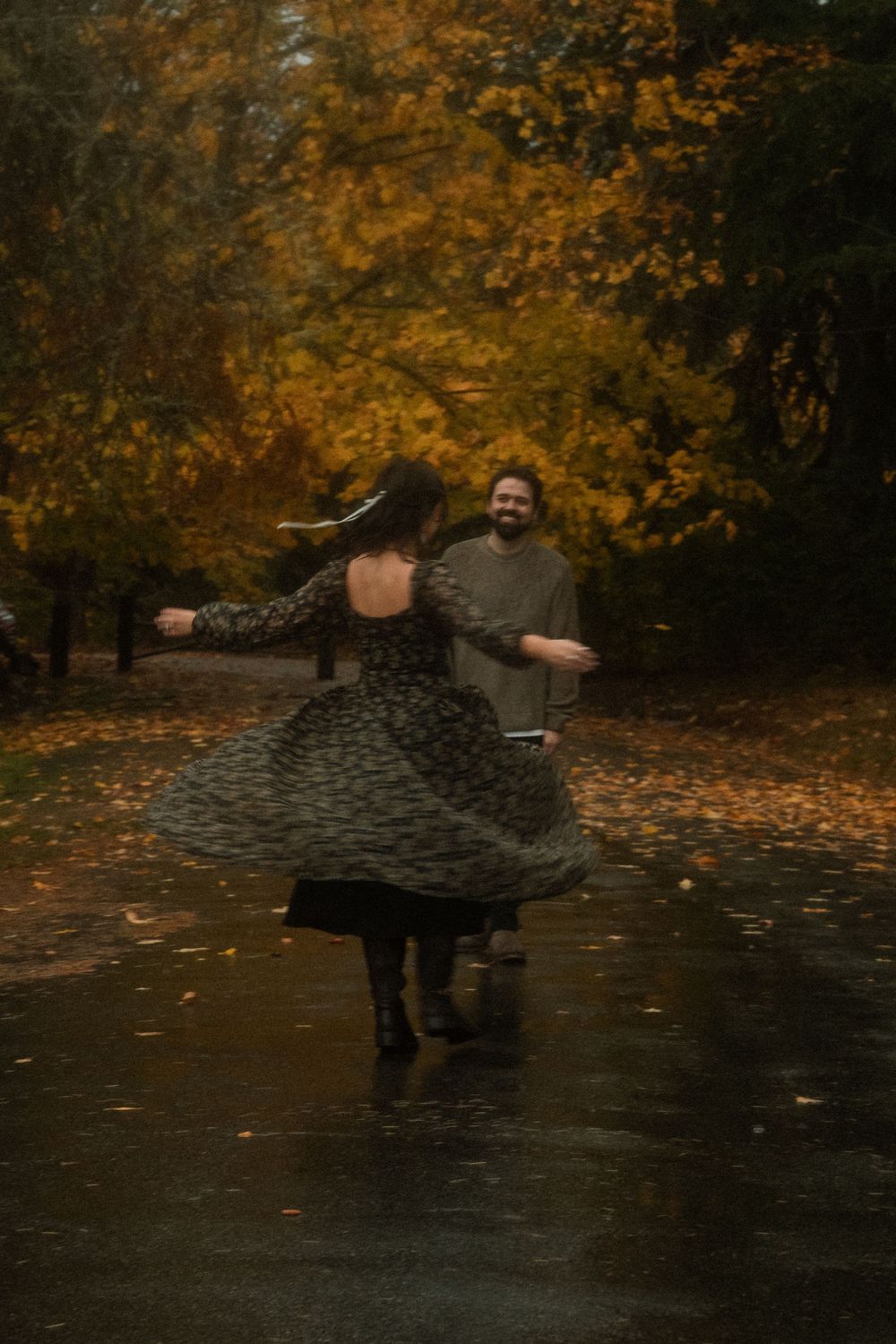 A person in dark clothing spins in a graceful dance motion against a backdrop of autumn trees with golden foliage.