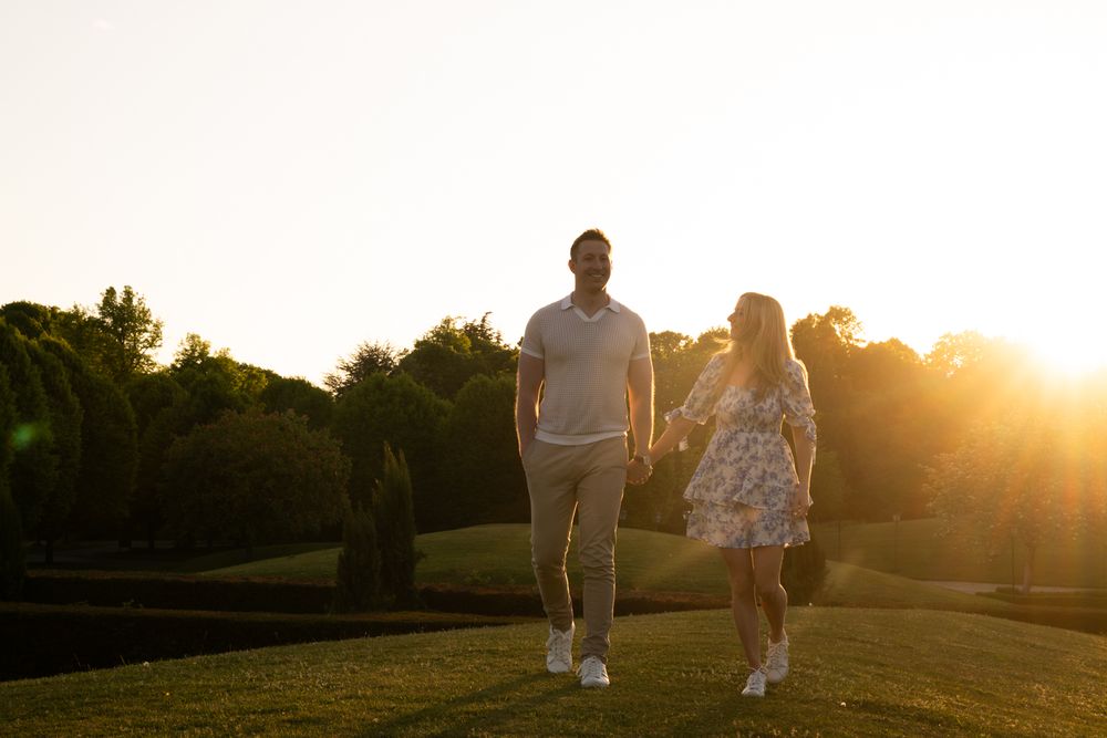 A couple walking hand in hand on a grassy hill during golden sunset hour.