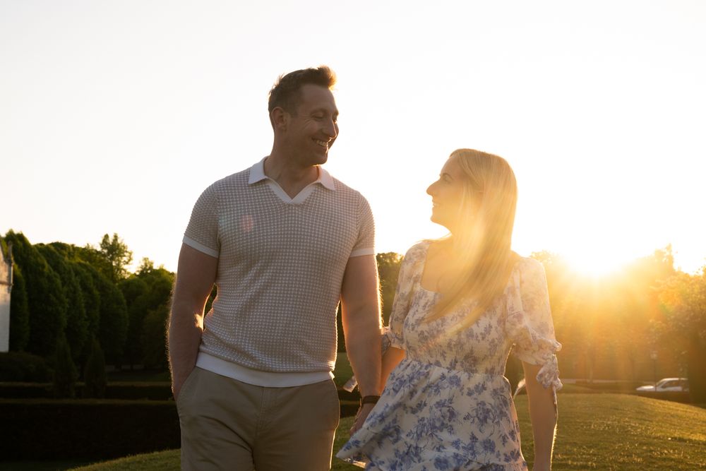 Couple walking together at sunset with golden sunlight streaming through trees in a romantic outdoor setting.