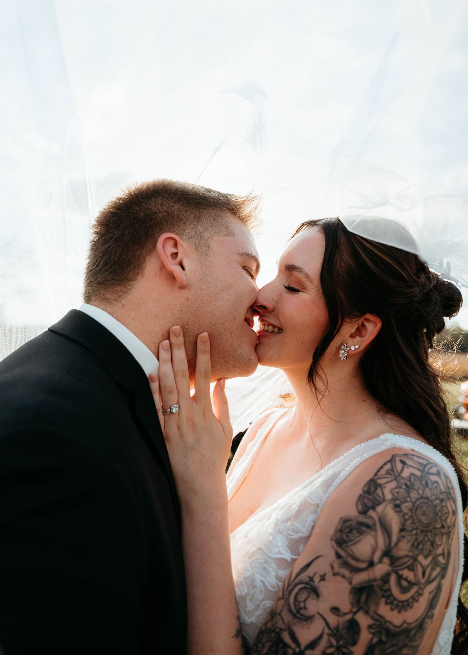 Close-up wedding photography showing intimate moment with bride's detailed lace dress and tattoos.