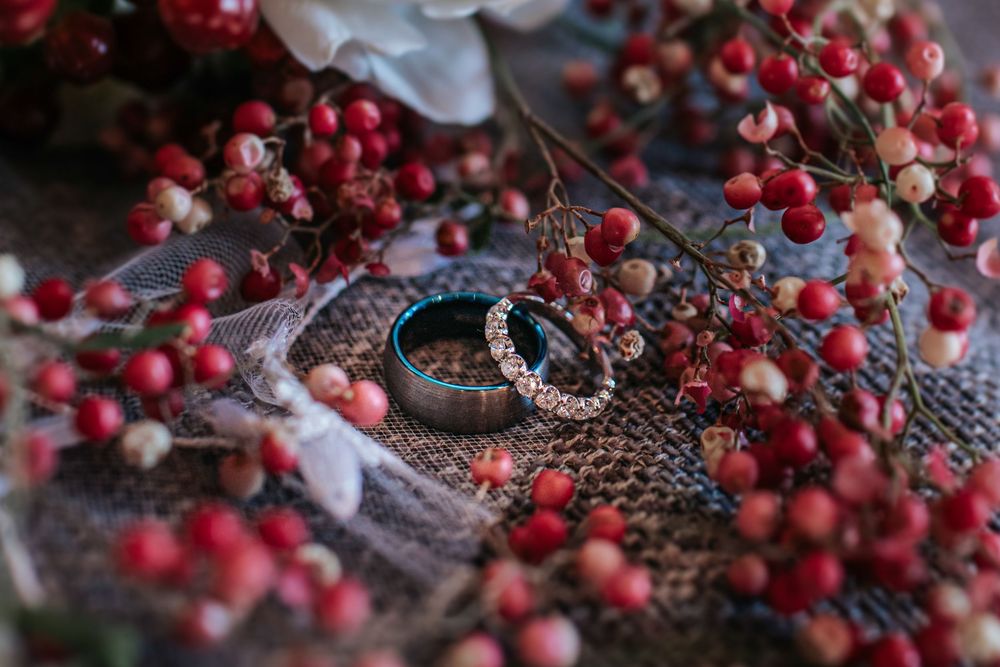 Wedding rings nestled among red berries and white flowers on textured fabric.