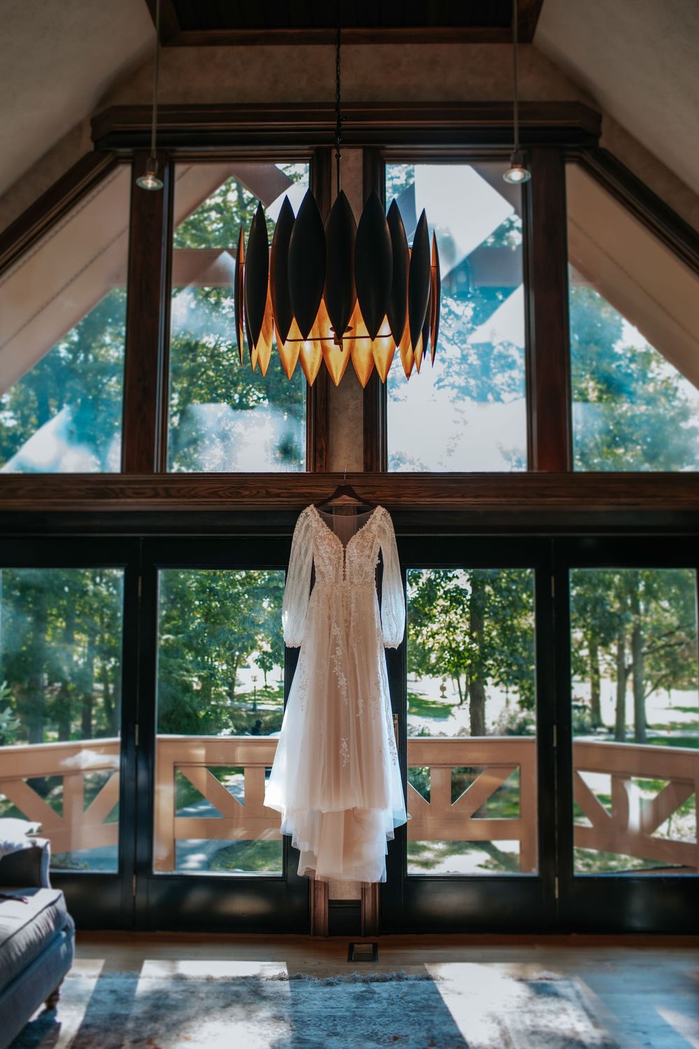 A wedding dress hanging beneath a modern geometric chandelier in a rustic venue.