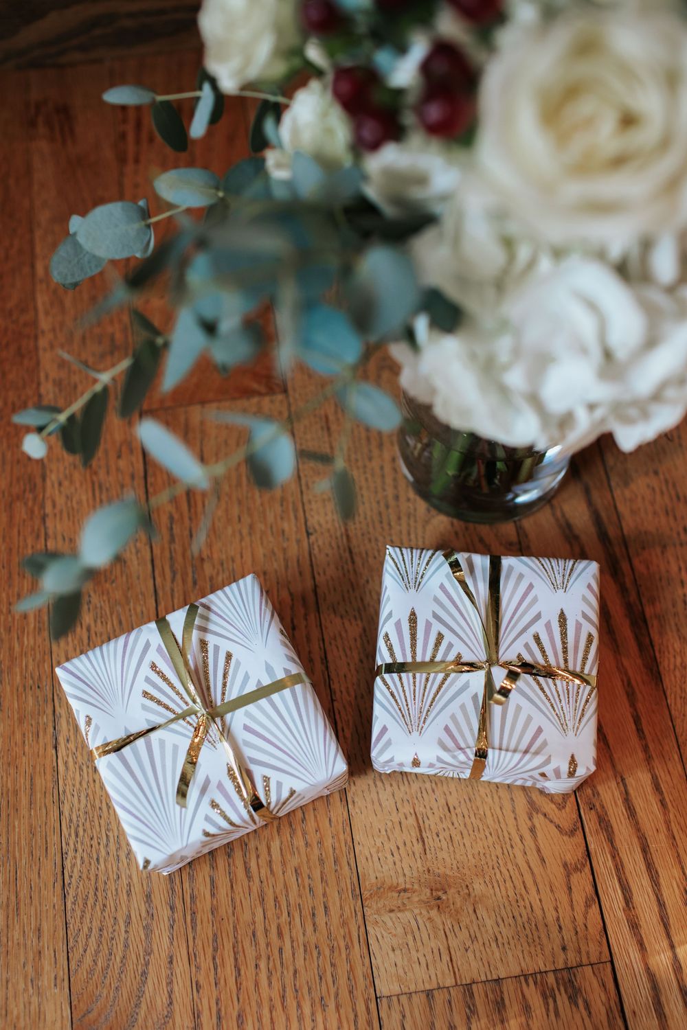Art deco style paper place cards with gold details arranged on wooden surface with white roses and eucalyptus.