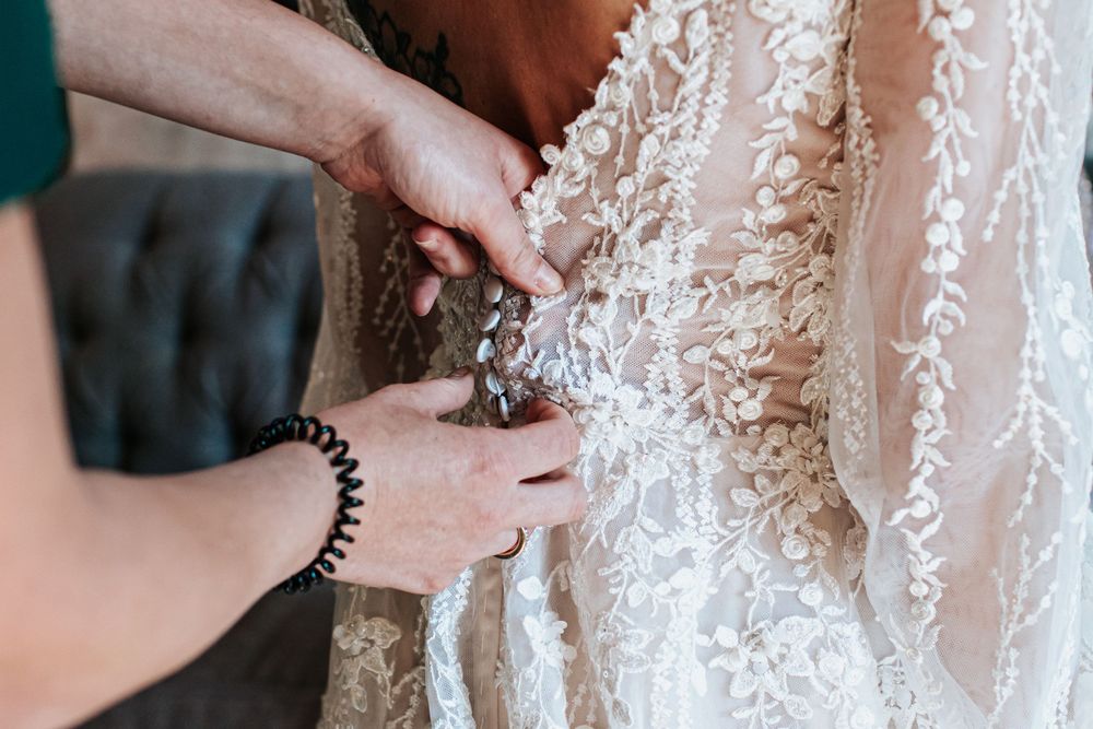 Hands fastening delicate buttons on an intricate lace wedding dress.