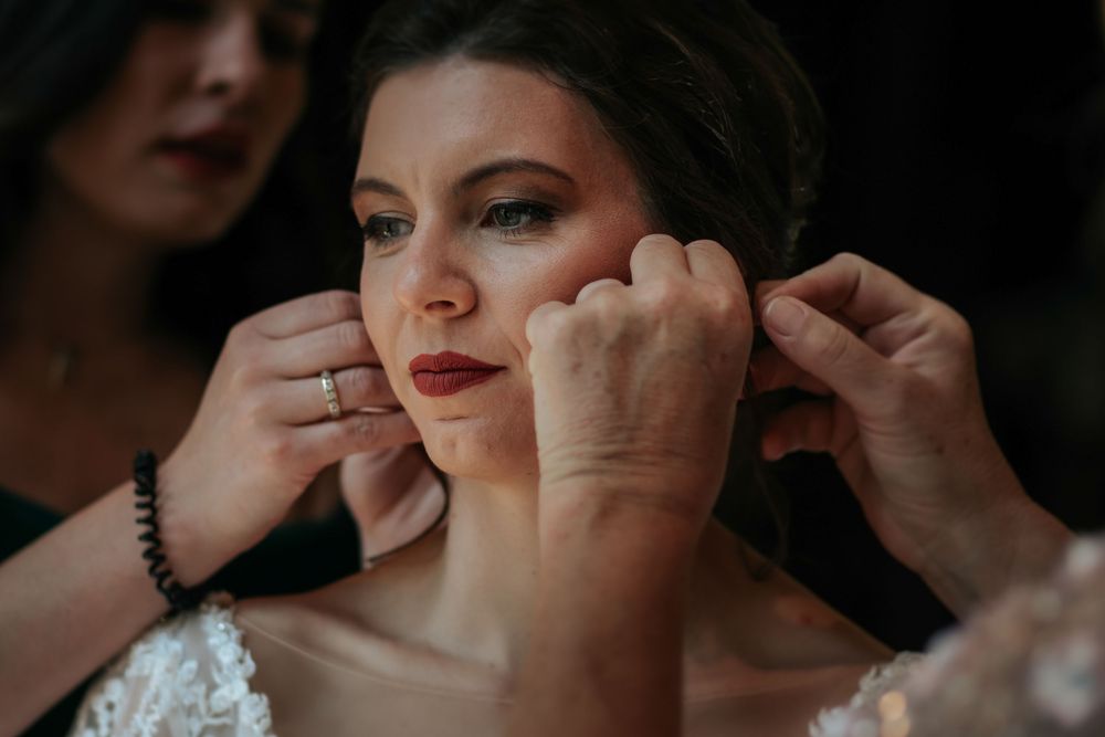 A close-up of hands helping with bridal earrings during wedding preparations.