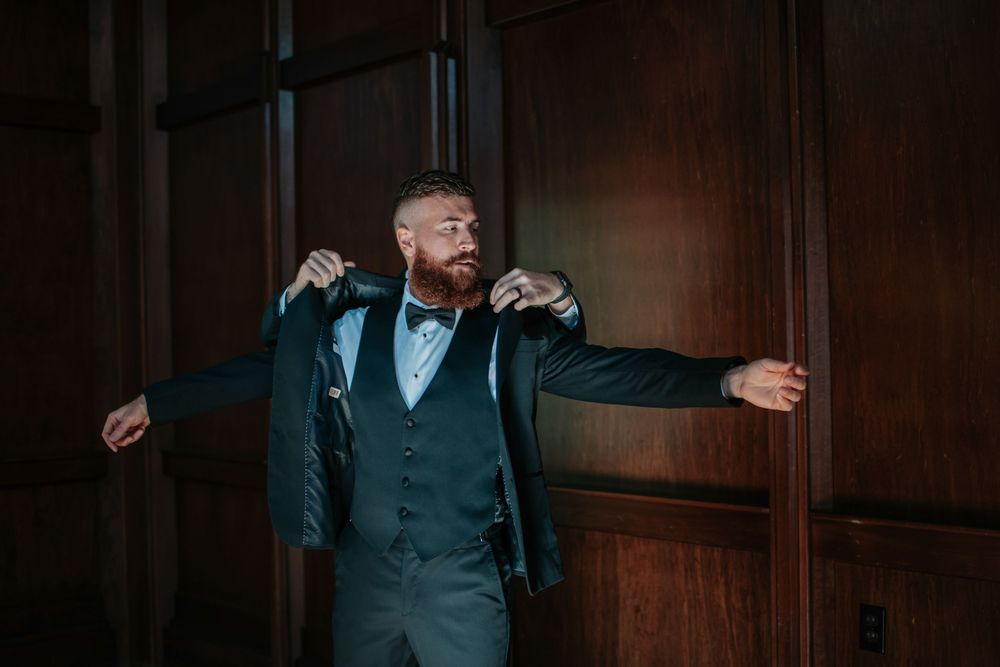 Groomsmen in dark suits sharing laughs in a dimly lit room.
