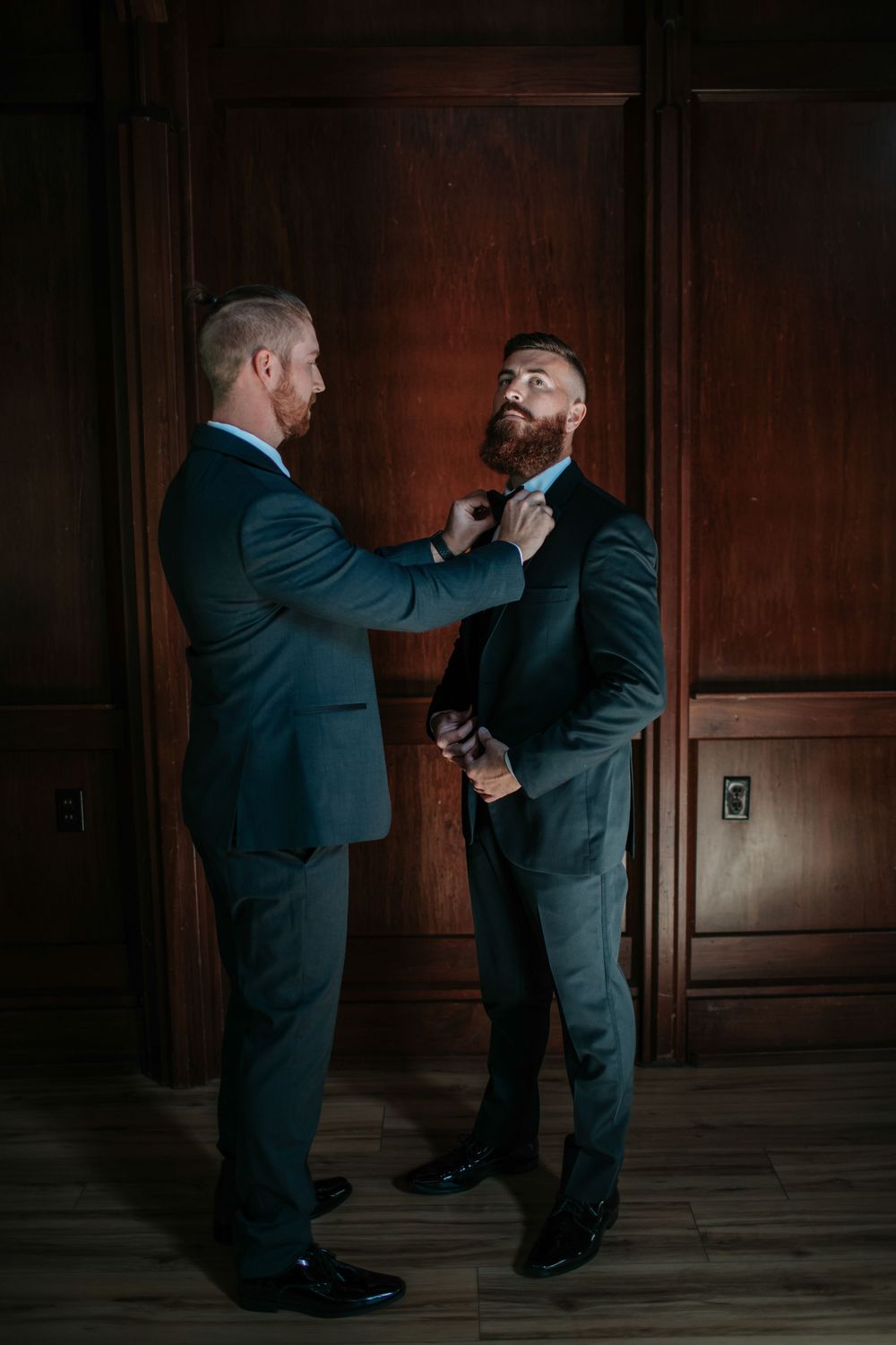 Wedding party members in suits playfully posing against wood paneled walls.