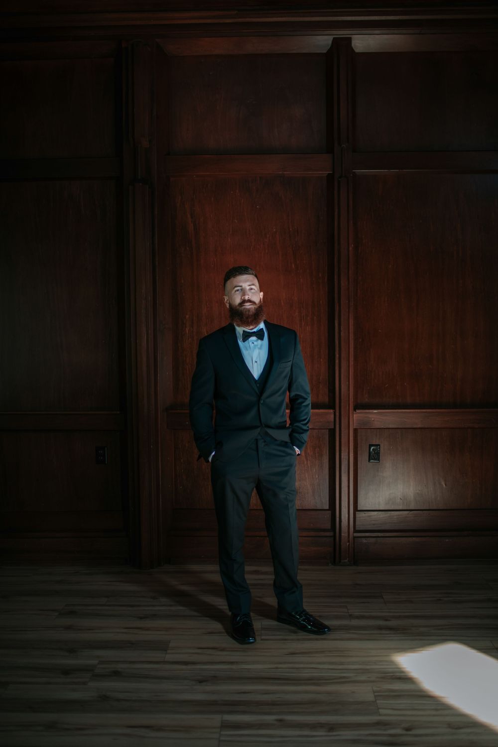 Dramatic portrait of formal attire against wood paneled wall with natural light streaming in.