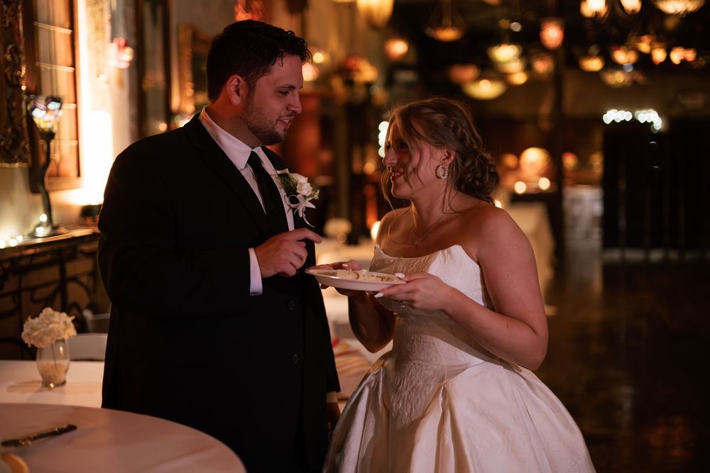 Bride and groom sharing wedding cake at elegant dimly lit reception venue.