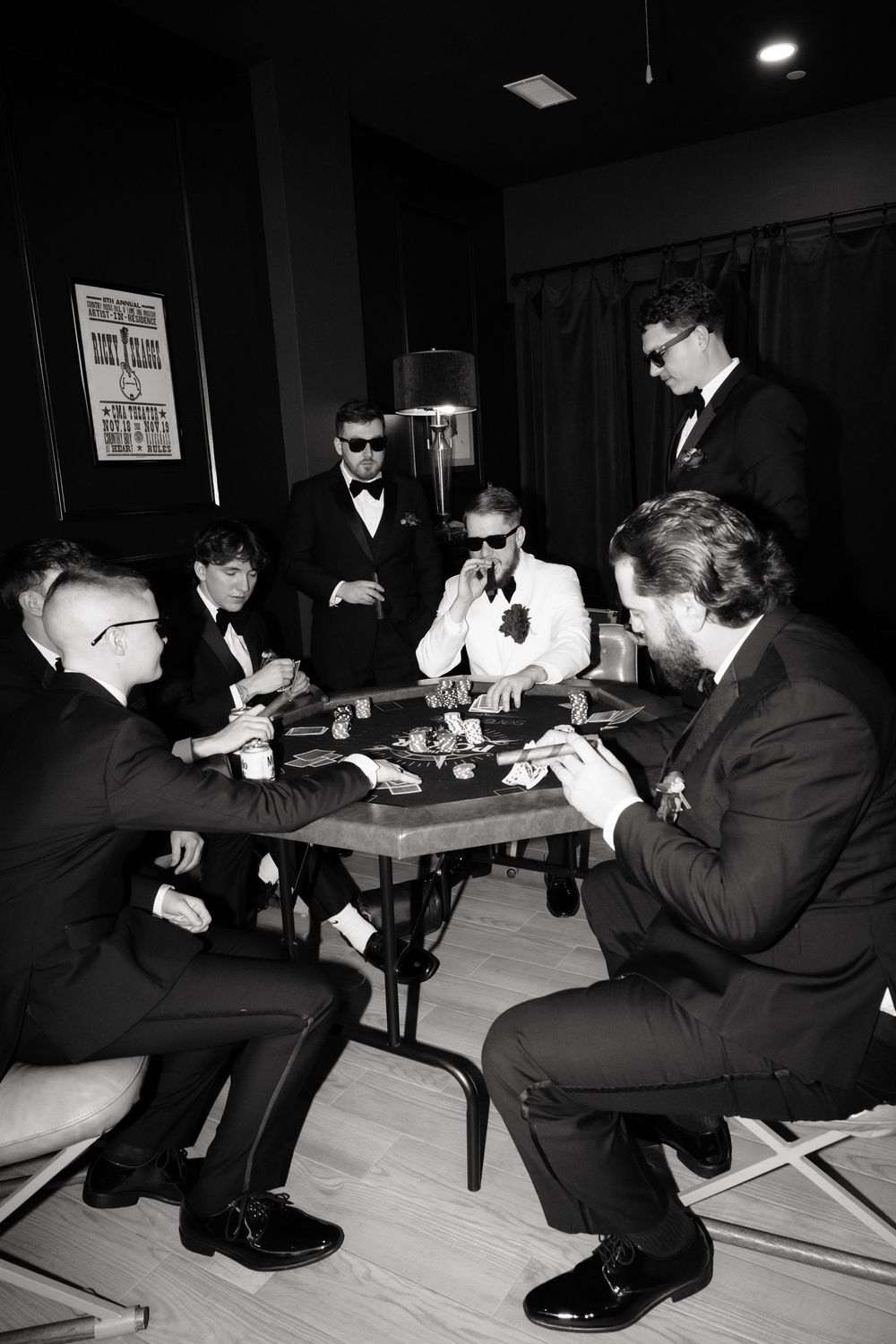 Group of men in formal suits playing poker at a table in a dimly lit room, black and white photo.