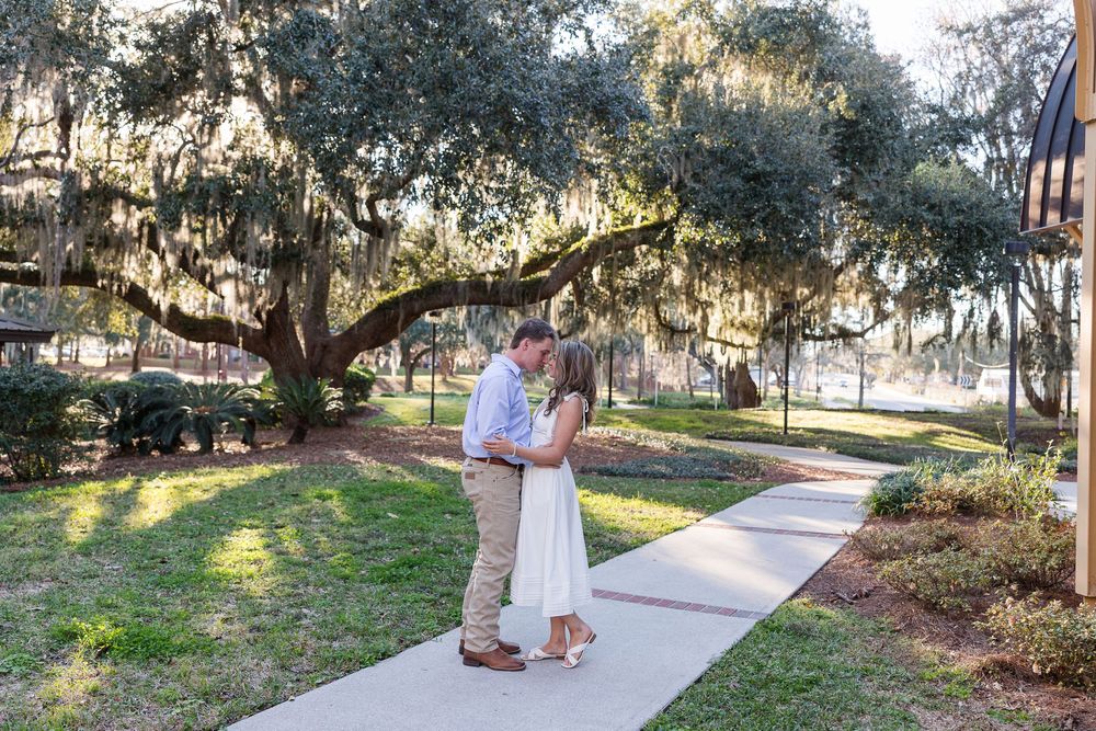 A couple walks along a scenic tree-lined path with Spanish moss hanging from the branches during golden hour.