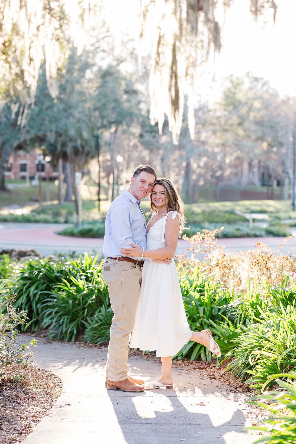 A couple shares a romantic moment in a garden path lined with yellow flowers and greenery.