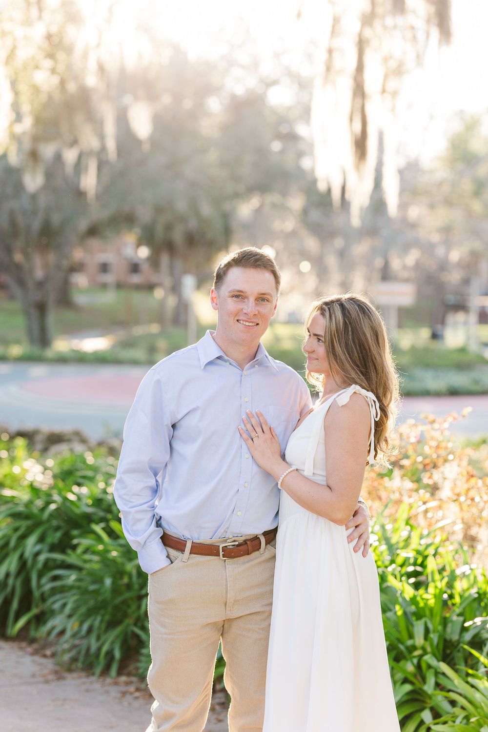 Couple in white and khaki taking romantic photos in a garden setting with flowering plants.