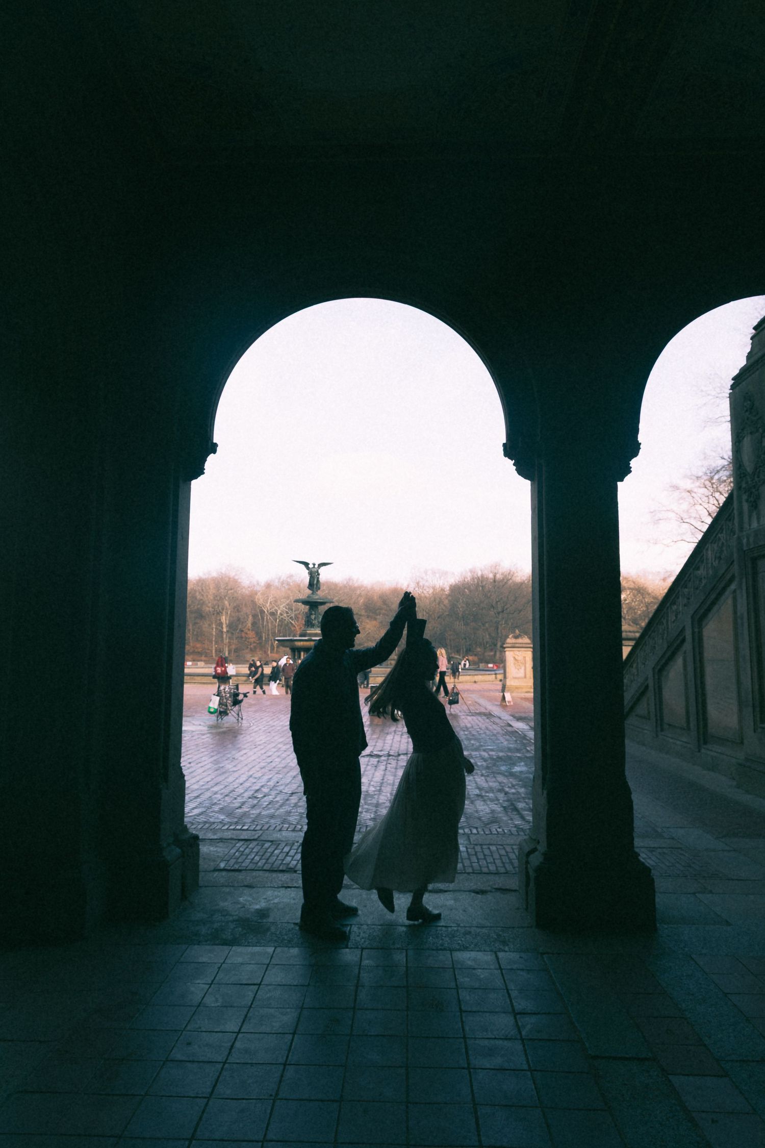 Silhouetted figures dance under an archway at sunset creating a dreamy atmospheric scene.