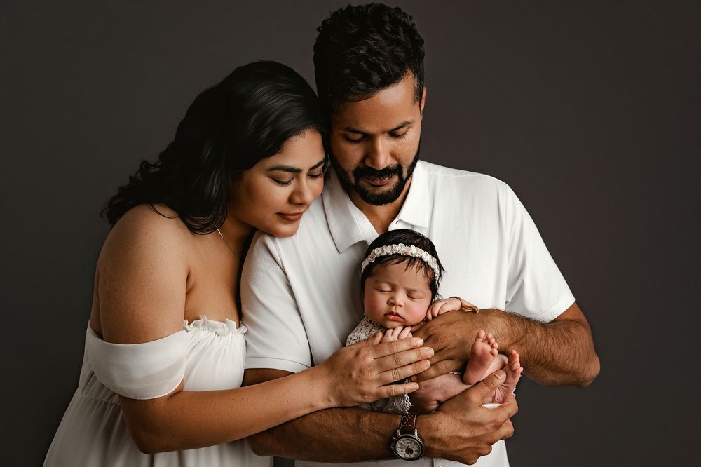 Family poses together in studio with newborn baby in dark and intimate setting.