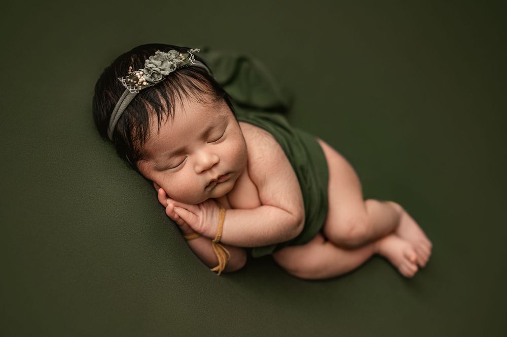 Sleeping newborn baby rests peacefully in dark green tones during professional photoshoot.