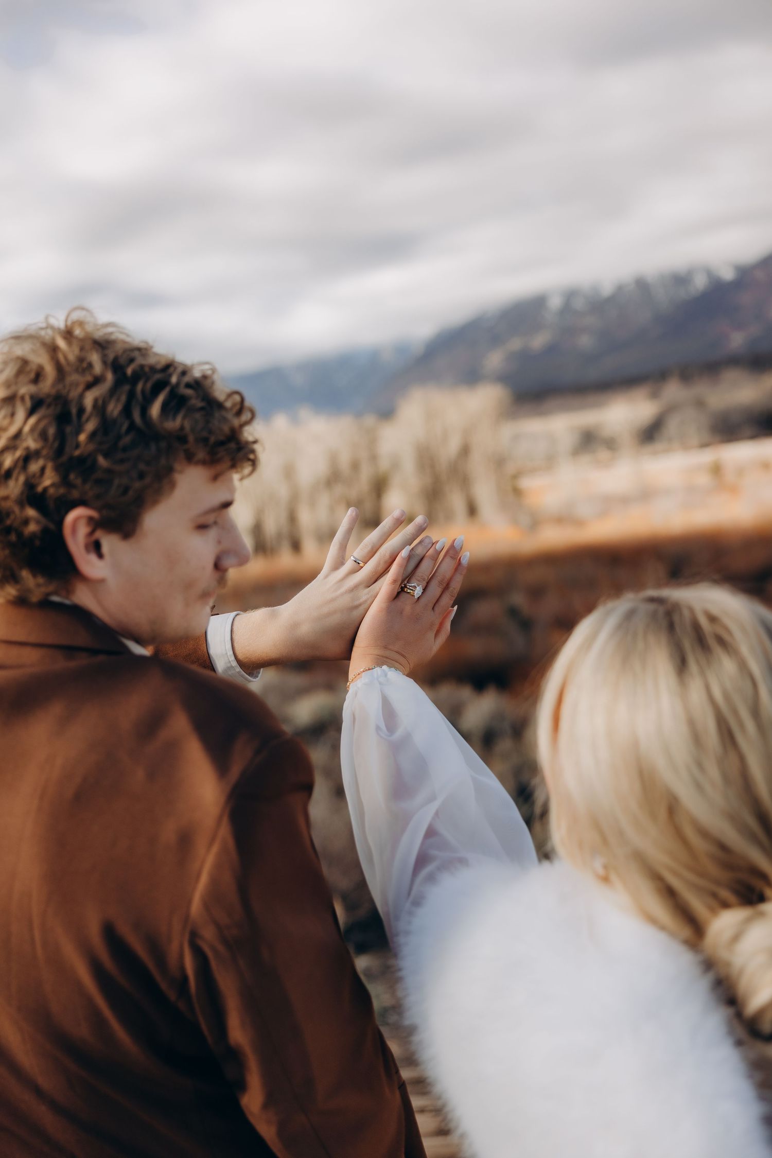 A couple shares a tender moment against a mountainous backdrop on their wedding day with dramatic cloudy skies.