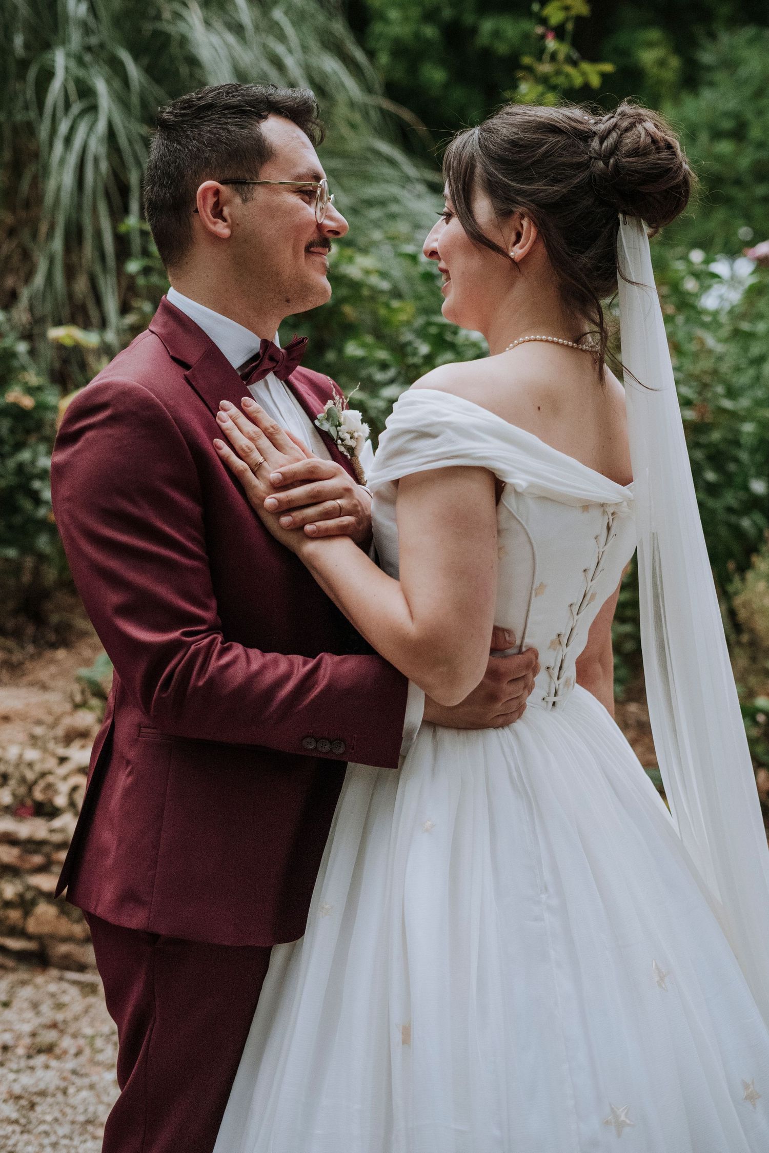 A couple in wedding attire walks hand in hand through a lush green park on their special day.