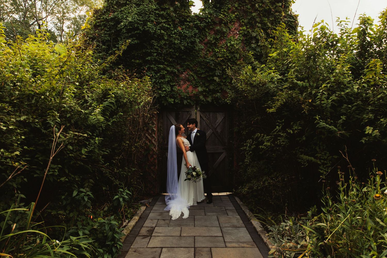 Stone pathway leads through a verdant garden setting at an outdoor wedding venue.